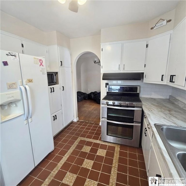 kitchen featuring arched walkways, stainless steel appliances, decorative backsplash, white cabinets, and under cabinet range hood