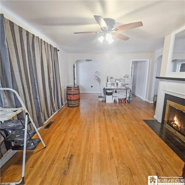 living room featuring arched walkways, a tiled fireplace, ceiling fan, wood finished floors, and baseboards