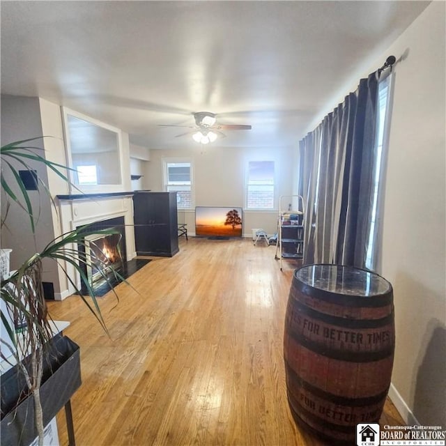 living room with light wood-style flooring, baseboards, a ceiling fan, and a fireplace with flush hearth