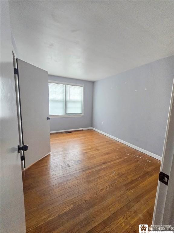 spare room with hardwood / wood-style floors and baseboards