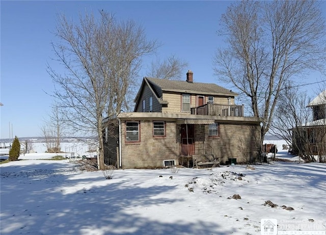 snow covered back of property featuring a chimney and brick siding