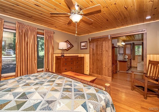 bedroom featuring wooden ceiling, a barn door, wood finished floors, and wainscoting