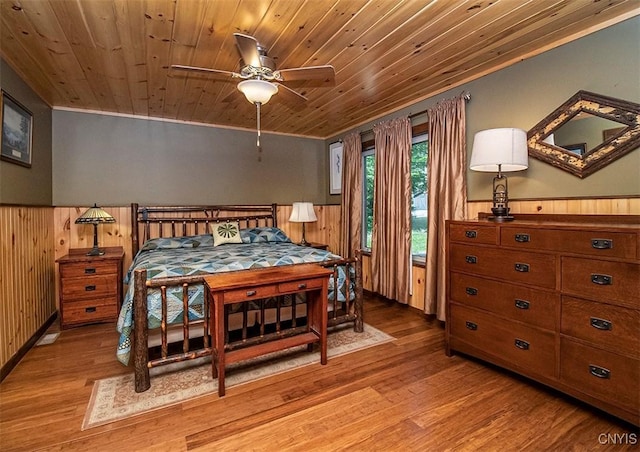 bedroom with a wainscoted wall, wood ceiling, and light wood-style floors