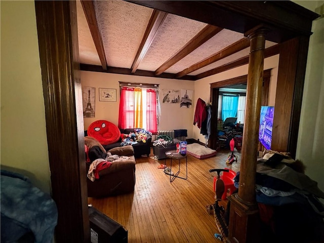 living room with a wealth of natural light, beamed ceiling, decorative columns, and hardwood / wood-style flooring