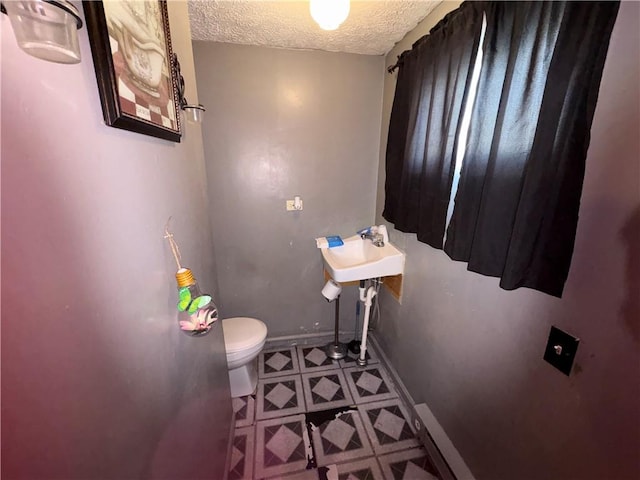 half bathroom with a textured ceiling, tile patterned floors, toilet, and baseboards