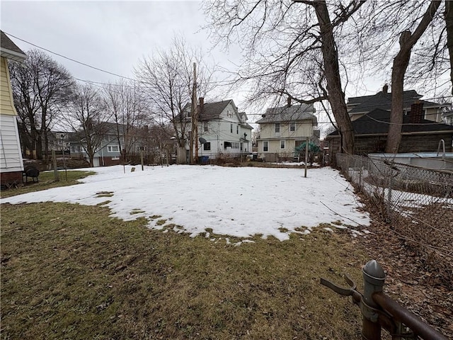 yard layered in snow with a residential view and fence