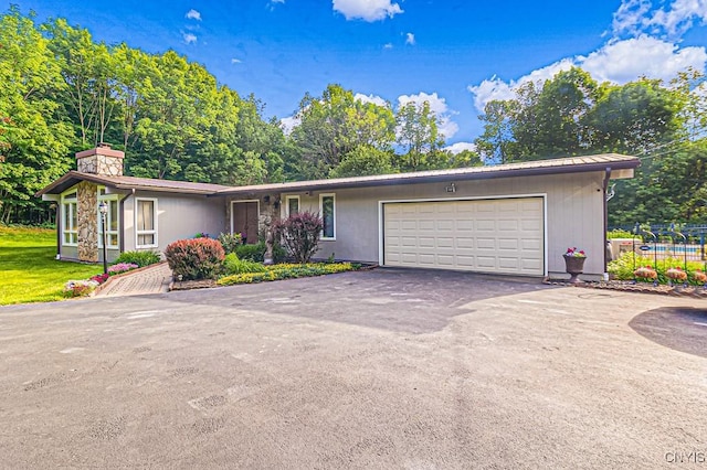 view of front of property featuring a chimney, an attached garage, a front yard, metal roof, and driveway