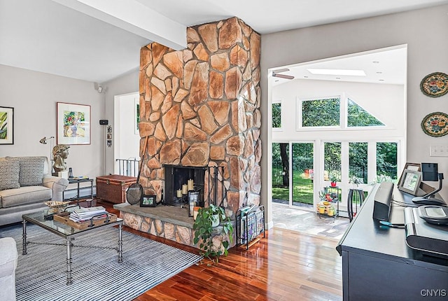 living area with a skylight, wood finished floors, a stone fireplace, high vaulted ceiling, and beam ceiling