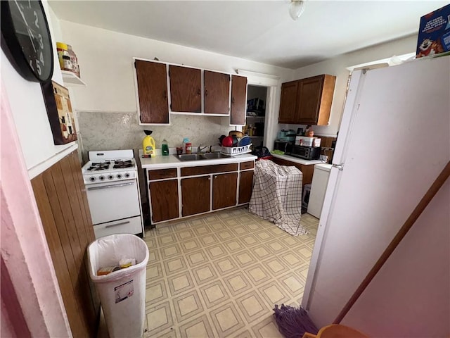 kitchen with a wainscoted wall, light floors, light countertops, white range with gas cooktop, and a sink