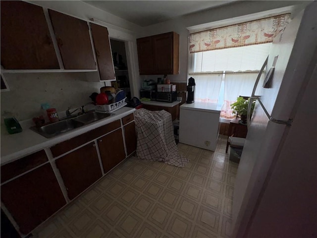 kitchen with light countertops, a sink, and freestanding refrigerator