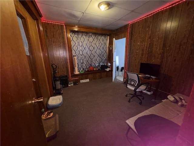 carpeted home office featuring wooden walls and a drop ceiling