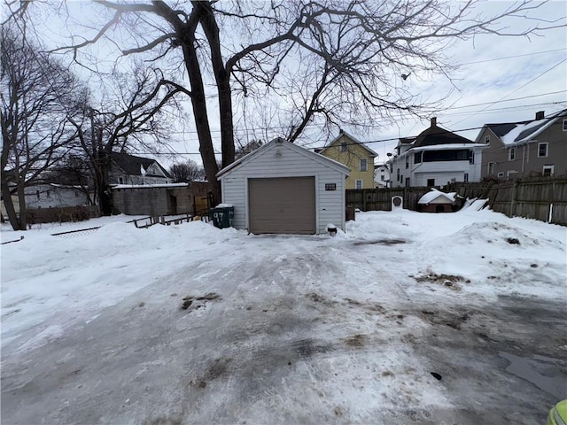 yard covered in snow featuring a residential view, a detached garage, fence, and an outdoor structure