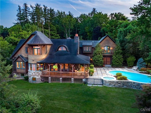 rear view of property featuring an outdoor pool, a yard, a chimney, and an in ground hot tub