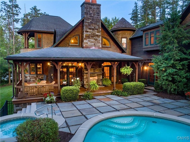 back of property with a shingled roof, a patio area, an outdoor pool, and a chimney