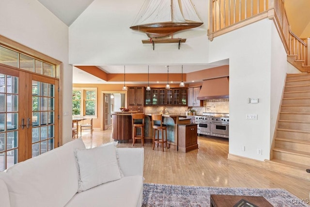 living room featuring french doors, light wood finished floors, stairway, a high ceiling, and baseboards