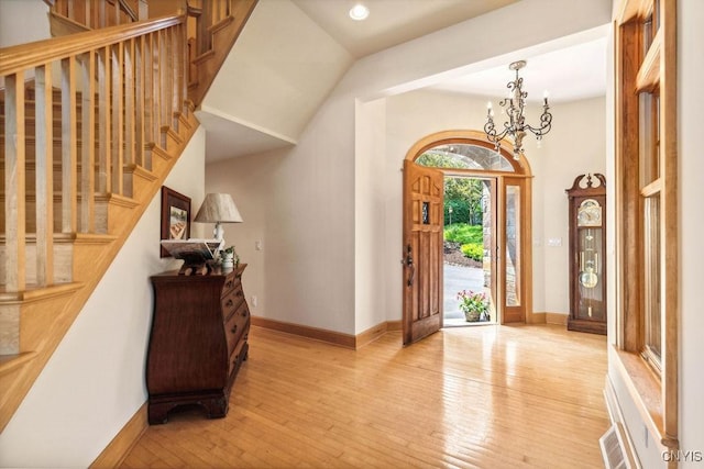 foyer featuring light wood finished floors, stairs, baseboards, and a notable chandelier