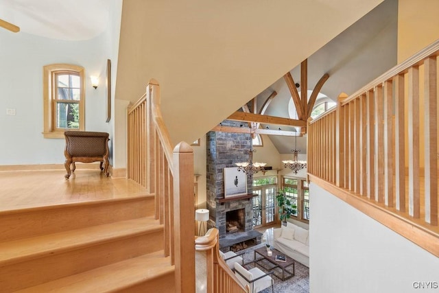 stairs with high vaulted ceiling, a healthy amount of sunlight, a notable chandelier, and a stone fireplace