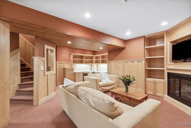 living room with built in shelves, light carpet, stairs, wainscoting, and a glass covered fireplace