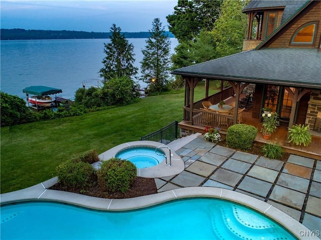 pool with a patio area, a water view, a yard, and an in ground hot tub