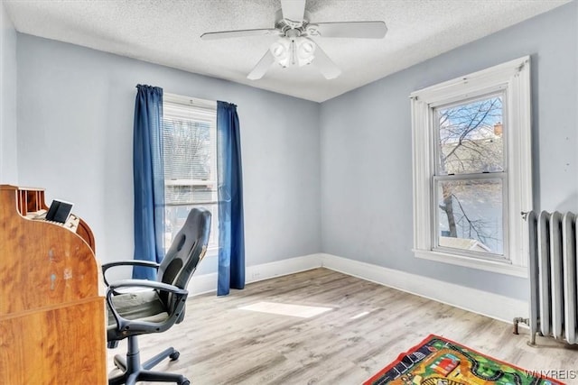 office area with baseboards, radiator, ceiling fan, wood finished floors, and a textured ceiling