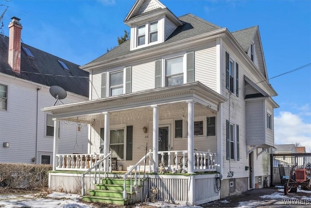 american foursquare style home with covered porch and a shingled roof