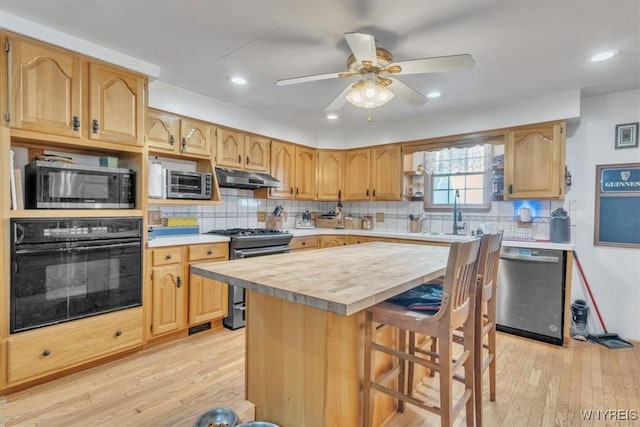 kitchen featuring light wood-style flooring, under cabinet range hood, stainless steel appliances, a sink, and decorative backsplash