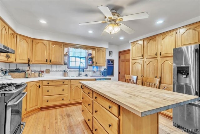 kitchen featuring light wood-style flooring, butcher block countertops, a sink, appliances with stainless steel finishes, and backsplash