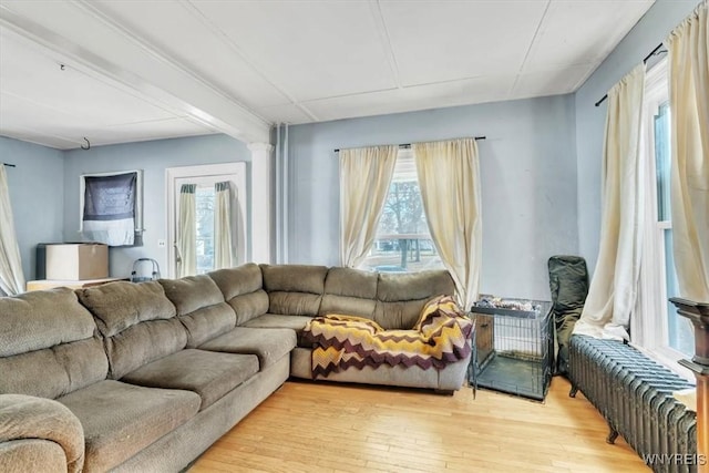 living room featuring light wood finished floors, radiator heating unit, and ornate columns