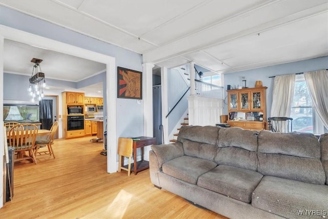 living room featuring light wood-type flooring, crown molding, ornate columns, and stairs