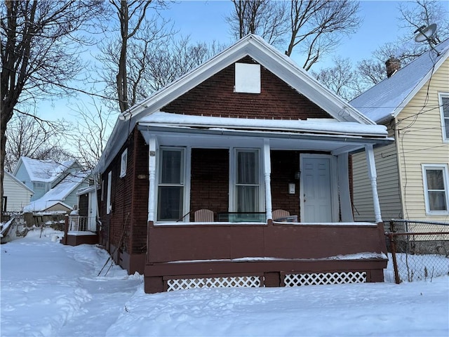 bungalow featuring fence, a porch, and brick siding