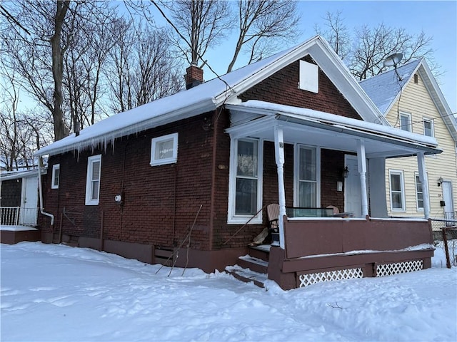 view of front of property with covered porch, a chimney, and brick siding