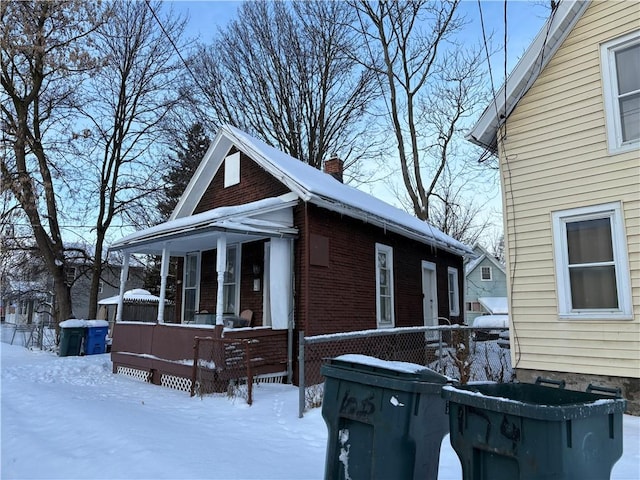 snow covered property with brick siding, a chimney, and a porch