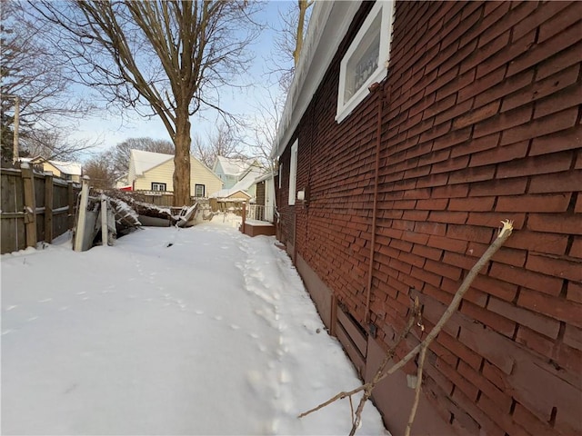 view of snow covered exterior featuring brick siding and fence