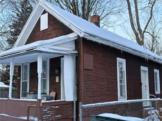 snow covered property featuring a porch, brick siding, fence, and a chimney