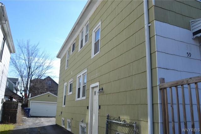 view of property exterior with a detached garage, fence, and an outbuilding