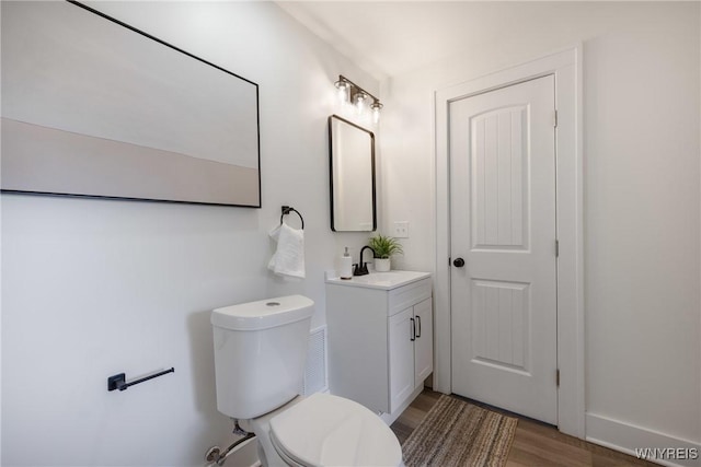 bathroom featuring toilet, baseboards, wood finished floors, and vanity