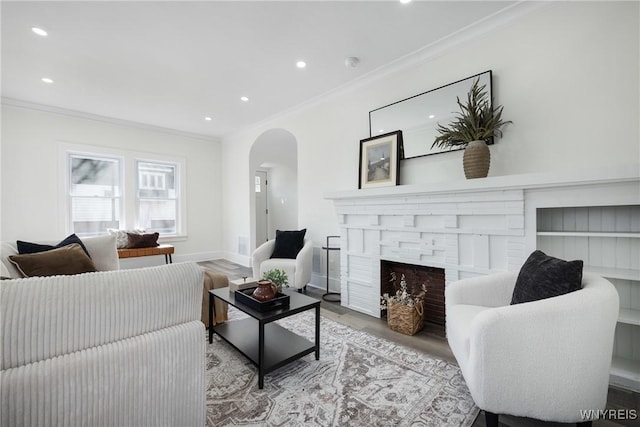 living area with ornamental molding, arched walkways, a brick fireplace, and wood finished floors