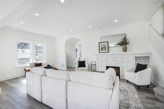 living room featuring baseboards, arched walkways, dark wood-type flooring, crown molding, and a fireplace