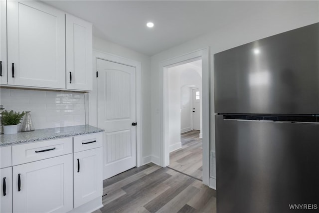 kitchen with backsplash, freestanding refrigerator, white cabinets, light stone countertops, and light wood-type flooring