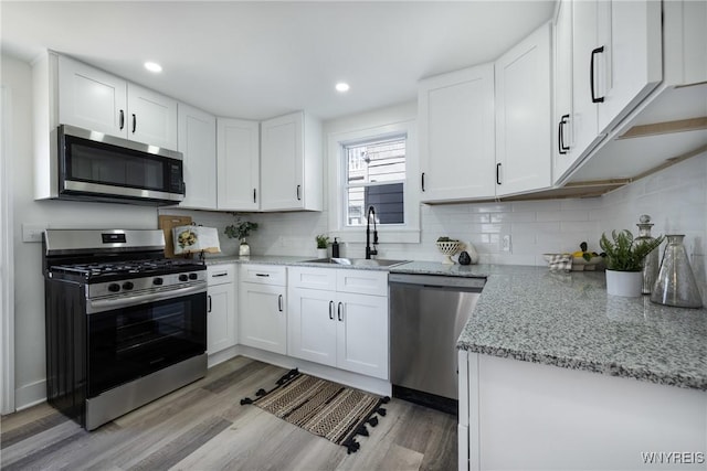 kitchen with appliances with stainless steel finishes, a sink, light wood-style flooring, and white cabinets