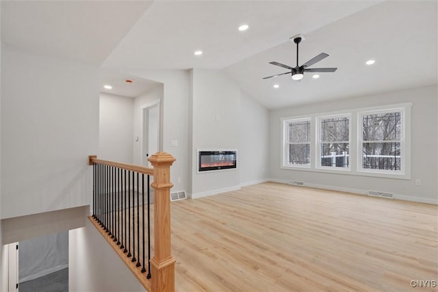 living room with a glass covered fireplace, visible vents, lofted ceiling, and light wood finished floors