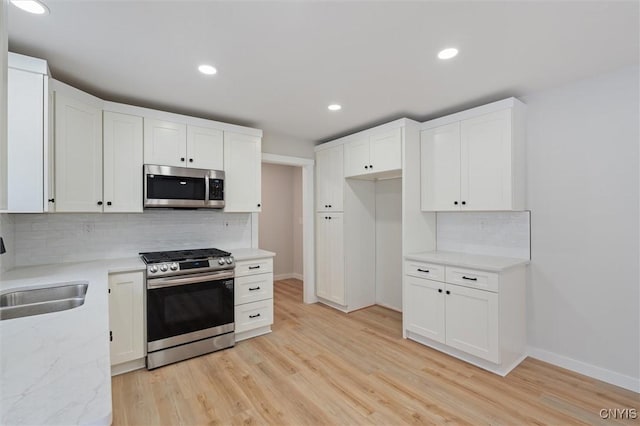 kitchen with appliances with stainless steel finishes, light wood-style floors, white cabinets, and a sink