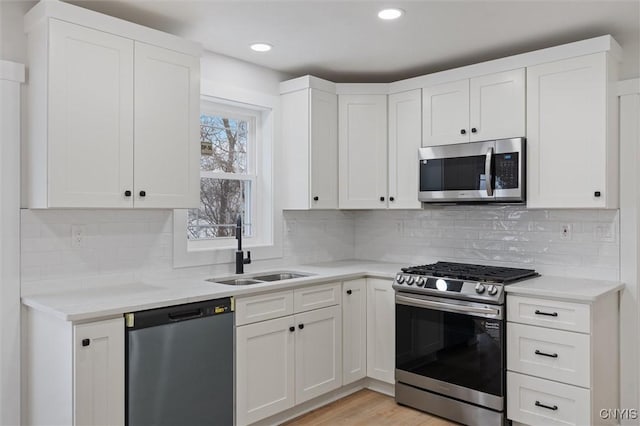 kitchen featuring light countertops, light wood-style flooring, appliances with stainless steel finishes, white cabinets, and a sink