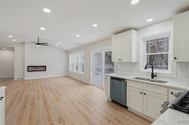 kitchen featuring lofted ceiling, a sink, stainless steel dishwasher, plenty of natural light, and a glass covered fireplace