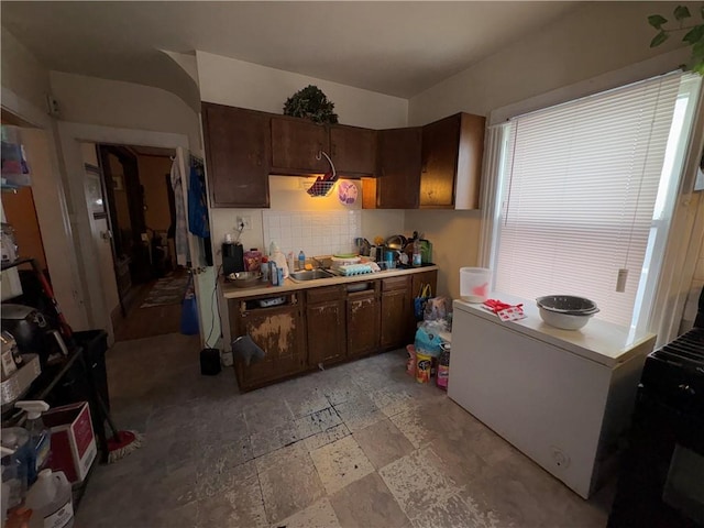 kitchen with tasteful backsplash, stone finish floor, light countertops, and a sink