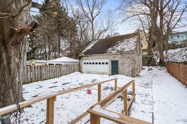 yard layered in snow with a detached garage, fence, and an outbuilding