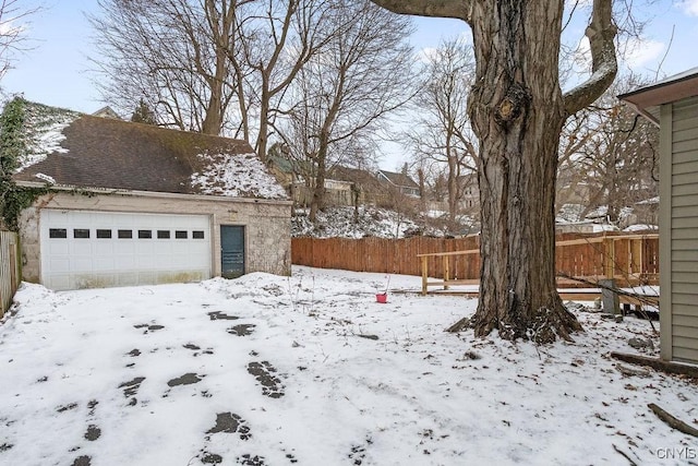 yard layered in snow featuring a detached garage, fence, and an outdoor structure