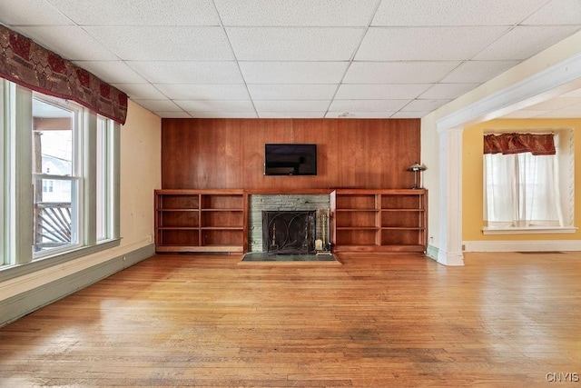 unfurnished living room with wooden walls, a fireplace, a paneled ceiling, and light wood-style floors