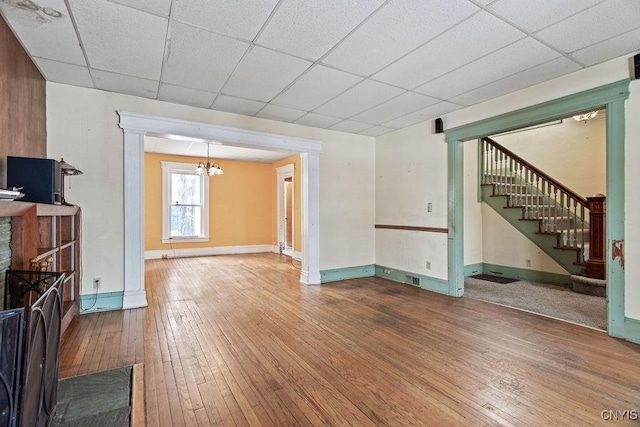 unfurnished living room with baseboards, a drop ceiling, stairway, hardwood / wood-style floors, and a fireplace