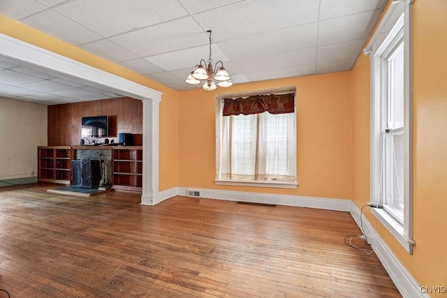 interior space with a fireplace with raised hearth, a drop ceiling, a notable chandelier, visible vents, and hardwood / wood-style floors